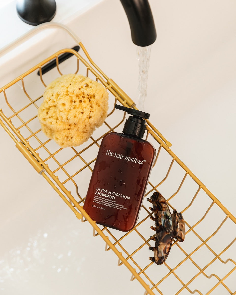 The Hair Method shampoo in a brass bath caddy under running water