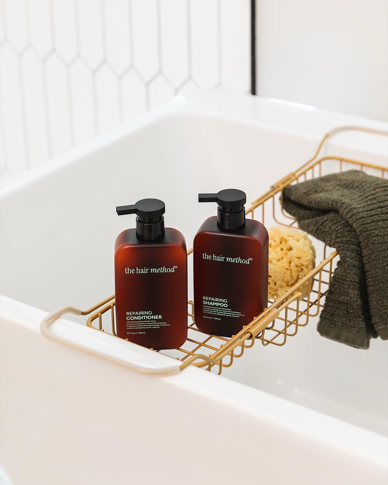 The Hair Method shampoo and conditioner in a brass caddy across a white bathtub